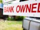 A sign in front of a home that says "Bank Owned"